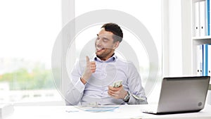 Happy businessman with money and laptop in office