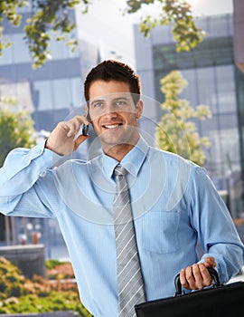 Happy businessman outside of office on phone