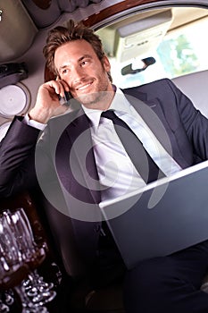 Happy businessman on phone call in limousine