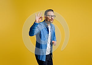 Happy businessman puckering lips and gesturing OK sign while standing against yellow background