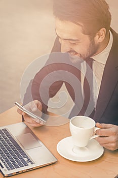 Happy businessman reading messages on mobile phone. Laughing man drinks coffee in street cafe and chatting on smartphone