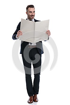 Happy businessman reading newspaper and smiling while walking