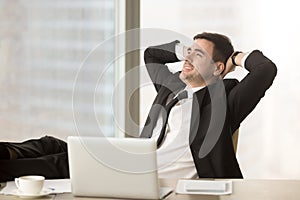 Happy businessman relaxing hands behind head near laptop, job do