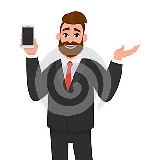 Happy businessman showing or holding smart phone, mobile, cell phone in hand and gesturing hand to copy space side away.