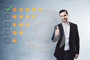 Happy businessman showing thumbs up to 5 star rating on concrete wall background. Customer service and excellent feedback