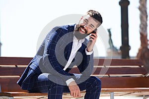 Happy businessman sitting on bench talking on mobile phone