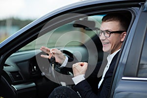 Happy businessman sitting in his new car and showing keys