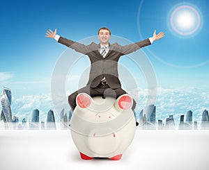 Happy businessman sitting on piggy bank