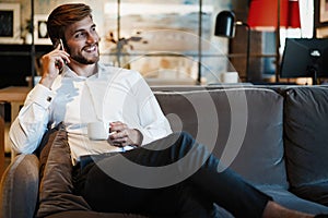 Happy businessman sitting and talking on the phone at office.