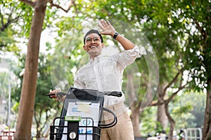 A happy businessman smiles and waves while pushing his bike, greeting someone while heading to work
