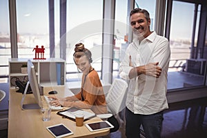 Happy businessman standing while female colleague working in office