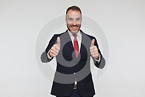 Happy businessman in suit with red tie making thumbs up gesture and smiling
