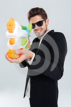 Happy businessman in sunglasses and suit shooting with water gun