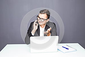 Happy young businessman talking on cell phone and using laptop in office