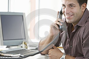 Happy Businessman Using Landline Phone In Office