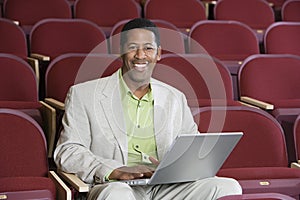 Happy Businessman Using Laptop In Auditorium