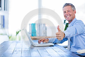 Happy businessman using laptop computer and looking at camera with thumbs up