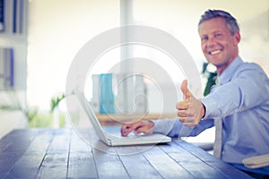 Happy businessman using laptop computer and looking at camera with thumbs up