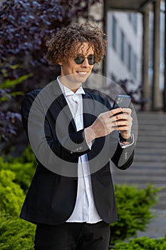 Happy businessman using smartphone typing text answering e-mail messages online mobile app outdoors