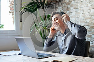 Happy businessman wearing headphones singing song at workplace, funny employee or freelancer using laptop, enjoying favorite track