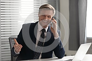 Happy businessman wearing suit laughing talking on phone in office