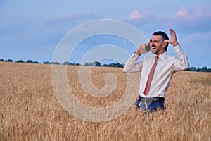 happy businessman in wheat field emotionally talking on the phone