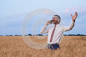 happy businessman in wheat field emotionally talking on the phone