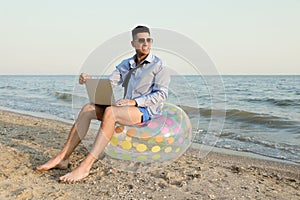 Happy businessman working with laptop on beach. Business trip