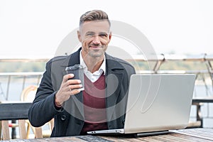 Happy businessman working in laptop drinking coffee in outdoor cafe
