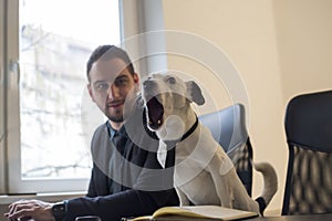 happy businessman working on laptop in office sitting next to dog with a tie