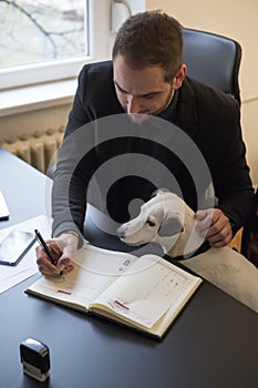 happy businessman working on laptop in office sitting next to dog with a tie