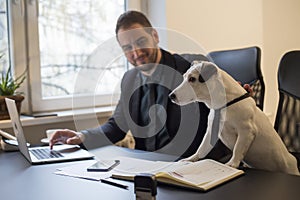 happy businessman working on laptop in office sitting next to dog with a tie