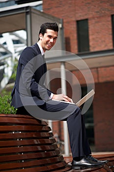 Happy businessman working on laptop outside the office