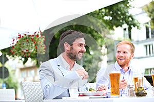 Happy businessmen having food at sidewalk cafe