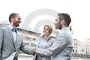 Happy businessmen shaking hands in city against clear sky