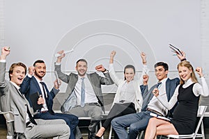 happy businesspeople with raised hands sitting on chairs at training