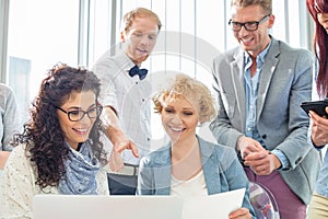 Happy businesspeople working on laptop in creative office