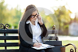 Happy businesswoman calling on mobile phone and taking notes outdoor