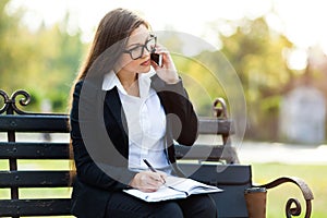 Happy businesswoman calling on mobile phone and taking notes outdoor