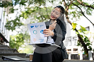 A happy businesswoman is checking the documents and talking on the phone while sitting on the stairs