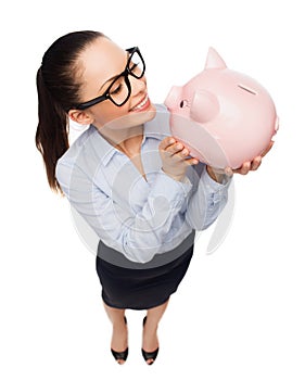 Happy businesswoman in eyeglasses with piggy bank