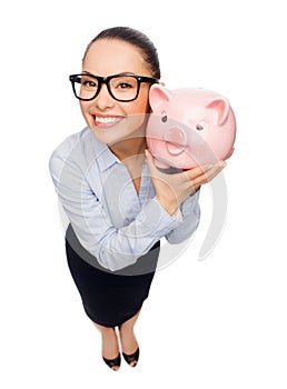 Happy businesswoman in eyeglasses with piggy bank