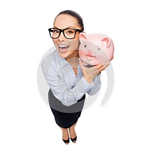 Happy businesswoman in eyeglasses with piggy bank