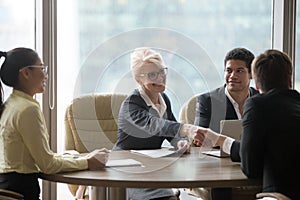 Happy businesswoman handshaking businessman over conference table at team meeting