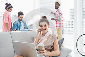 Happy businesswoman phoning and using laptop on couch