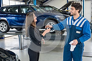 Happy Businesswoman Receiving Car Key From Mechanic At Garage