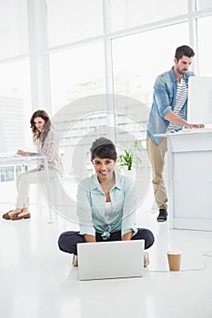 Happy businesswoman sitting on the floor using laptop