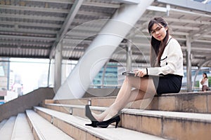 Happy businesswoman sitting on sidewalk.