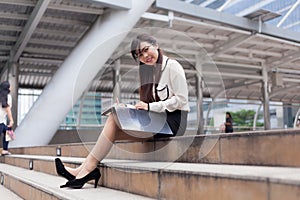 Happy businesswoman sitting on sidewalk.