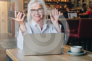 Happy businesswoman sitting at table in front of laptop, holding hands up and smiling, working, learning